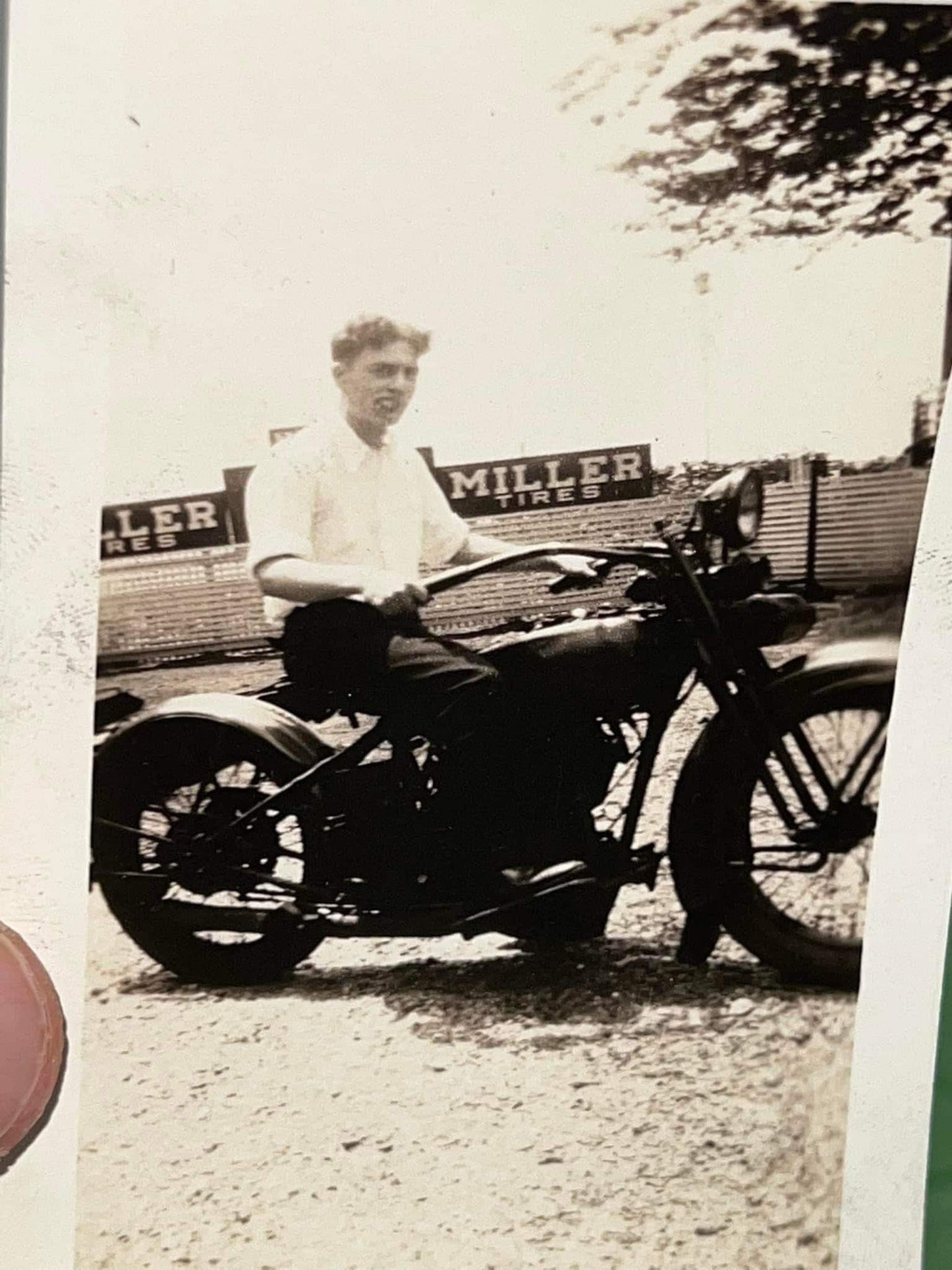 Vintage photography 1940s snapshot Man on a Harley or Indian appears to have a cigar in mouth Miller tires sign in background