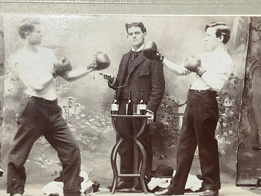 Antique mounted photo staged boxing match w table of booze 1900s