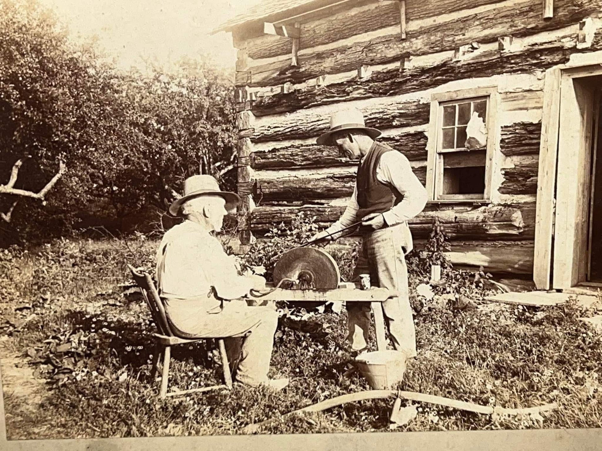 Antique photo 1890s rural occupational 2 farmers outside log cabin using grind wheel to sharpen sye blade